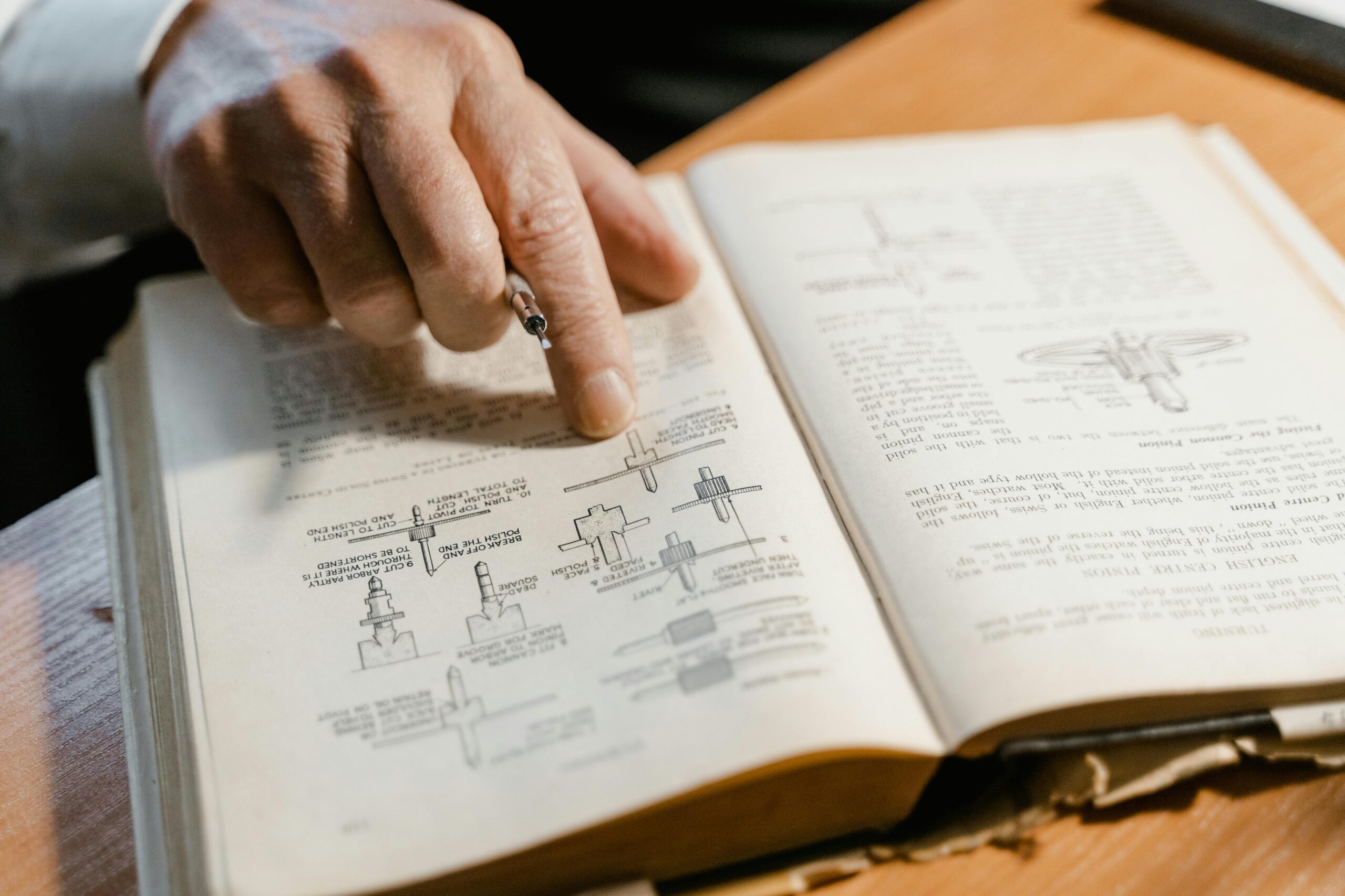 A hand points to a diagram in an open book focused on engineering concepts, highlighting learning.